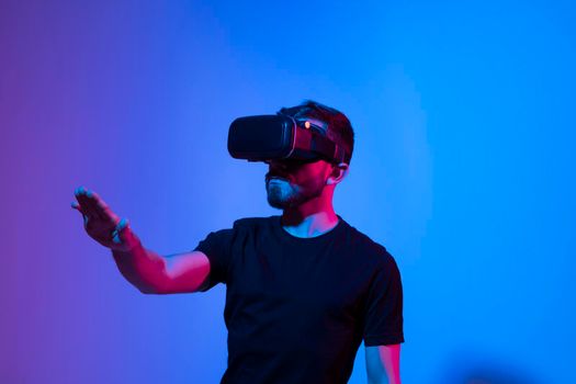 Young bearded man in virtual reality helmet plays online game in metaverse with a friends. Future technology concept