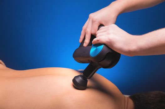 Close-up of male hands doing massage with a percussion massager on the back of a male client.