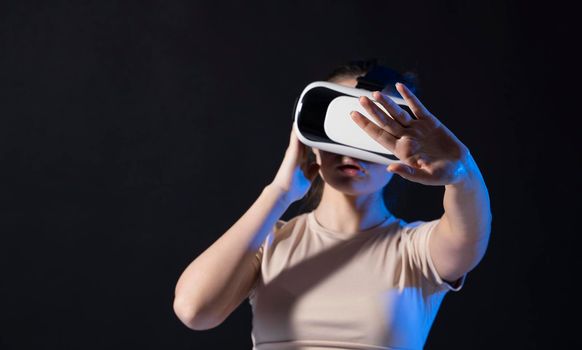 Close up of young woman stands in studio wearing VR glasses with a hand in air and trying to touch someting in virtual space. Virtual reality technology