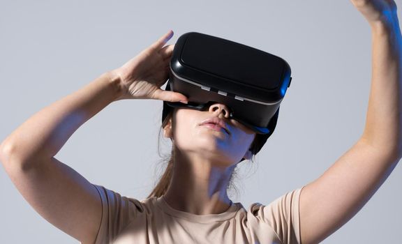 Young brunette woman wearing a virtual reality headset goggles and playing a game with a friends in metaverse. Future technology concept