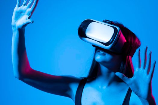 Young woman stands in studio wearing VR glasses and swiping scrolling zooming with hands in a virtual space while interacting with a objects in a metaverse. Virtual reality technology