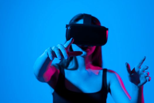 Young brunette woman in black t-shirt wearing VR goggles and interacts with cyberspace using swipe and stretching gestures while working on a project