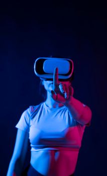 Modern architect using virtual reality glasses at workplace and touch something in virtual world. Woman working in VR goggles in neon light. Designer working in VR studio