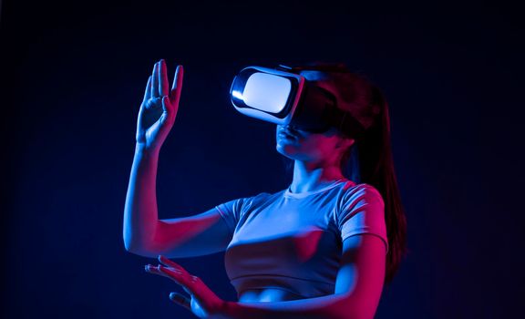 Future technology concept. Young woman wearing vr headset and watching 360 videos in neon light. Woman toching virtual objects in vr glasses