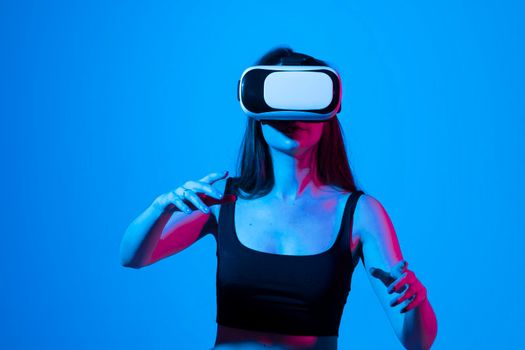 Young brunette girl in black t-shirt playing online games with a friends using VR glasses. Enjoying virtual reality headset while gaming with a friends in metaverse in neon light