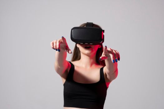 Brunette woman in a black t-shirt and VR headset looking up and trying to touch objects in virtual reality with both hands. Future technology concept