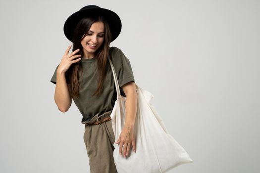 Happy beautiful brunette woman with white cotton bag in her hands. Girl holding textile grocery bag with vegetables. Zero waste concept