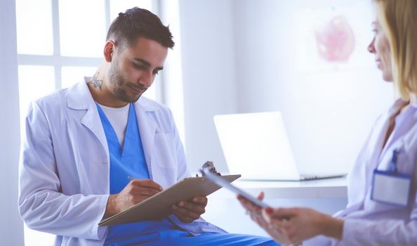 Handsome doctor is talking with young female patient and making notes while sitting in his office.