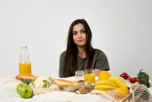 Happy woman in green t-shirt with a mesh eco bag with healthy vegan vegetables, fruits, bread and snacks. Healthy eating vegetarian concept