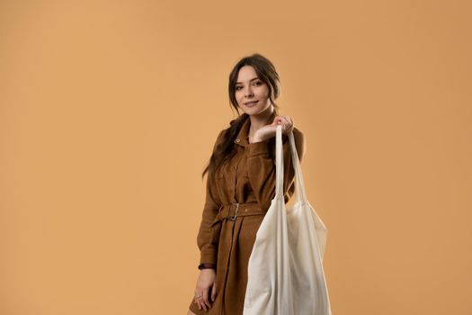 Young attractive beautiful sexy brunette woman holding reusable mesh bag with organic groceries over orange background. Zero waste, plastic free concept. Eco lifestyle. Conscious consumption