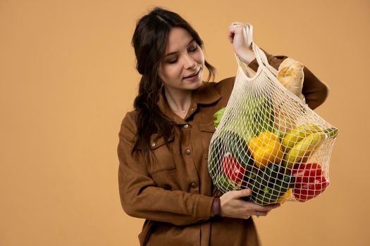 Zero waste concept. Young brunette woman in summer dress holding reusable cotton shopping mesh bag with groceries from a local market. Concept of no plastic. Zero waste, plastic free