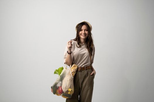 Concept of no plastic. Zero waste, plastic free. Sustainable lifestyle. Happy woman in a beige t-shirt and a hat holding reusable cotton shopping bag with organic groceries, bread and greens