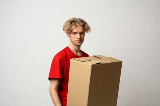 Cheerful delivery man holding a cardboard boxes and smiling while standing against white background. Courier holding a cardboard box in front of himself