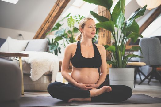Young beautiful pregnant woman training yoga, caressing her belly. Young happy expectant relaxing, thinking about her baby and enjoying her future life. Motherhood, pregnancy, yoga concept