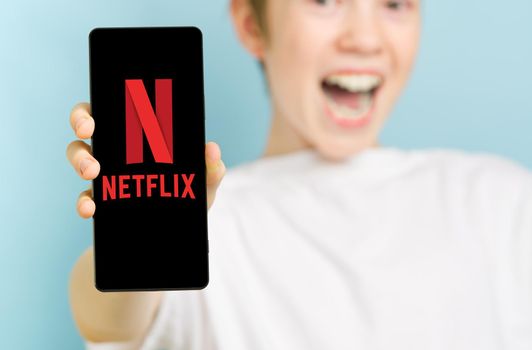 February 2022 - Tallinn, Estonia. Unfocused happy smiling boy with smartphone showing netflix app logo. Social media