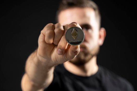 Successful businessman in black t-shirt with ethereum coin isolated on black background in studio. Hold ethereum, bitcoin, future currency