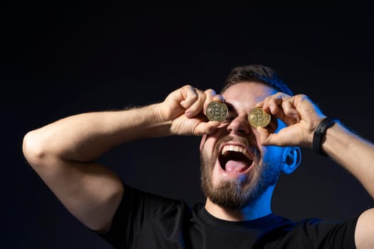 Crazy happy bitcoin lover with golden coin by eyes on the black background. Digital symbol of a new virtual currency. Cryptocurrency. Future payment system