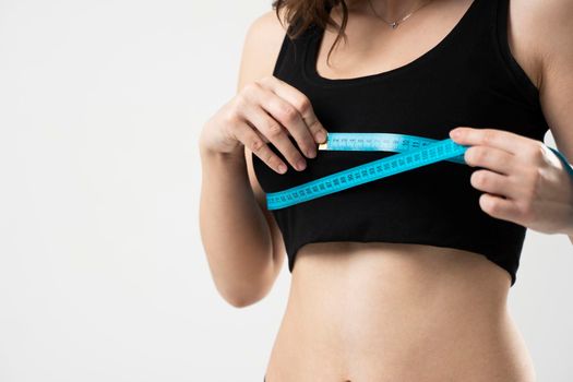 Beautiful sporty slim young woman measuring her figure size with tape measure. Womans holding centimeter and measuring a breasts with a blue measure tape