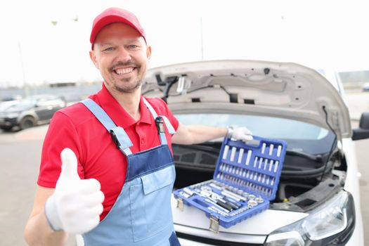 A man in a red uniform opened the hood of a car on the street, close-up. Tools for repairing a broken engine in a automobile