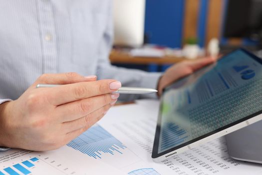 In female hands, a tablet with financial indicators, close-up. Stock reports, sale of shares, financial fund