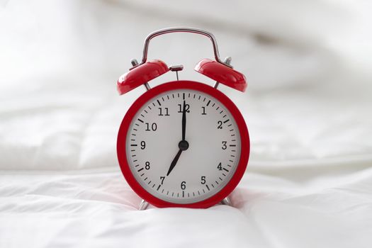 Red alarm clock on white bed linen, close-up. Wake me up hotel concept, morning sleep, bedtime