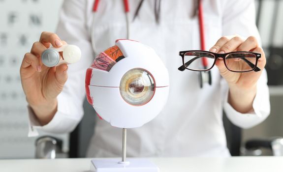 In female hands glasses for vision are next to the model of the eye, close-up. Protection of lenses from ultraviolet radiation