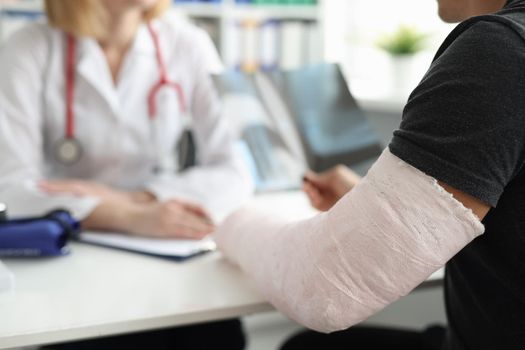 A man with a broken arm sits in front of a doctor, close-up, blurry. Traumatology consultation, trauma treatment