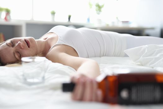 Drunk woman sleeping on a bed with a bottle, close-up. Female alcoholism, loneliness and stress