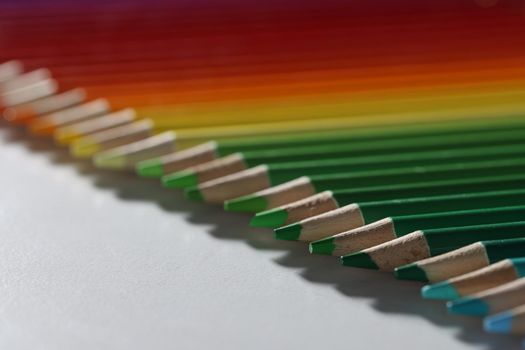 Colored pencils lie in a row on the table, close-up, blurry. Color palette from green to red. Education