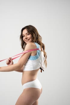 Happy attractive beautiful brunette woman in white underwear with a pink measuring tape stretched over body, in a white background
