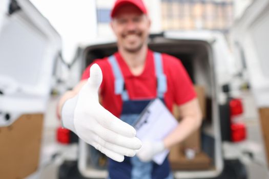 A courier in a red uniform holds out his hand, close-up, blurry. Address delivery of goods, postal services