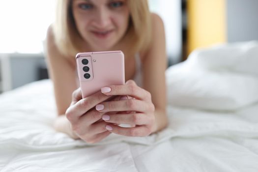 Beautiful blonde lies on the bed with a smartphone, close-up, blurry. Woman 30 years old reads online, internet in a hotel