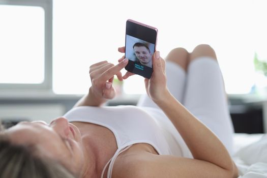 A woman lies on her back on the bed and looks into the phone, close-up. Dating site, search for a marriage partner online