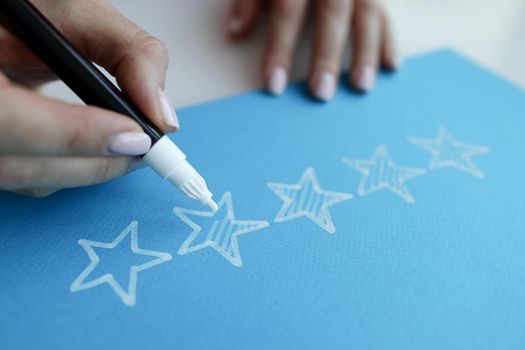 Woman hand painting over stars on blue paper for evaluating work closeup. Quality service concept