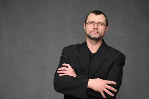 Portrait of a business man in glasses with crossed arms on a gray background