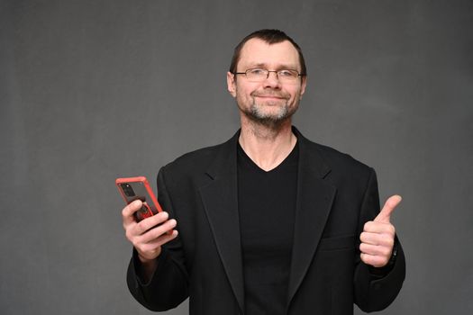 portrait of an adult man in glasses and a jacket with a phone shows ok