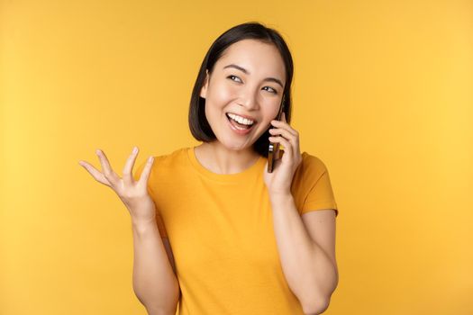 Young korean girl talking on mobile phone. Asian woman calling on smartphone, standing over yellow background.