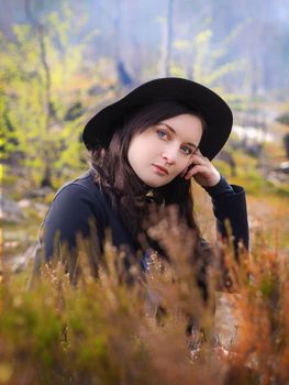 Portrait of a young girl in the autumn forest. Girl in a hat on a background of heather.