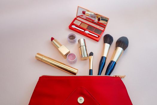 Top view of cosmetics standing out from red cosmetic bag on pink background. Photo