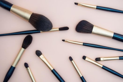 Assortment of female make-up of various face brushes. A set of professional dark blue and golden makeup brushes on a pink background. photo