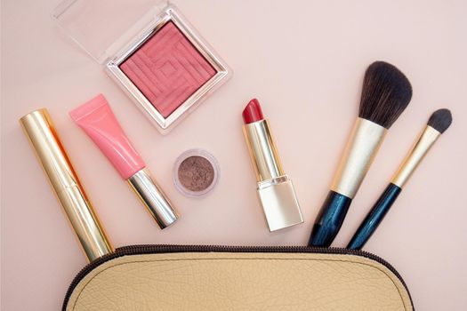 Top view of cosmetics standing out from beige makeup bag on pink background. Photo