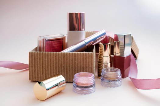 a set of cosmetics for a female face and eye makeup in a brown craft box on a pink background. photo