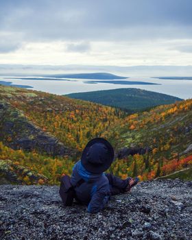 A woman in a hat on a mountain slope looks through binoculars in autumn against the backdrop of a lake and mountains. view from the back. photo