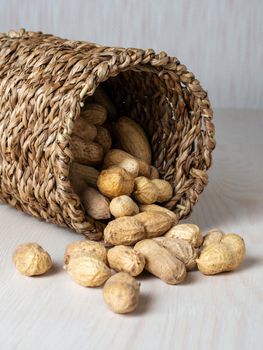 Shelled peanuts in a small wicker basket on a white background. Peanuts full from a wicker basket. Peanuts spill out of a wicker basket. photo