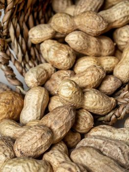 Shelled peanuts in a small wicker basket on a white background. Peanuts full from a wicker basket. Peanuts spill out of a wicker basket. photo