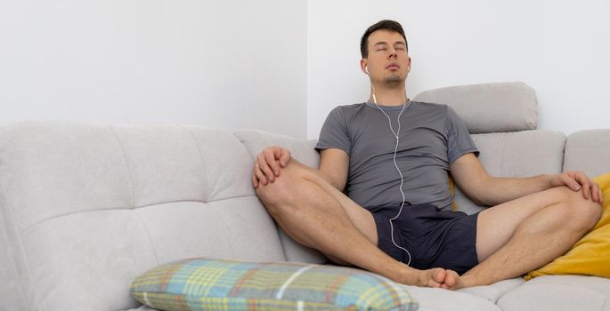 young man in headphones meditating on couch. High quality photo