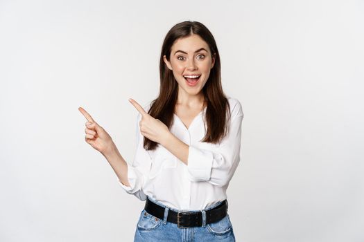 Portrait of enthusiastic smiling woman, female entrepreneur pointing fingers left and showing advertisement, showing announcement, white background.