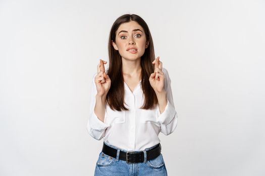 Hopeful woman praying, cross fingers for good luck, begging, yearning smth, standing over white background. Copy space