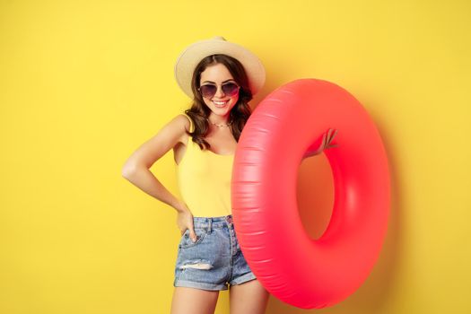Stylish beach girl with swimming ring, laughing and smiling on summer vacation, sea trip, standing happy against yellow background.