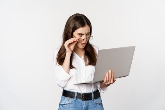 Shocked woman looking at laptop screen confused, stunned about smth on computer, standing over white background.